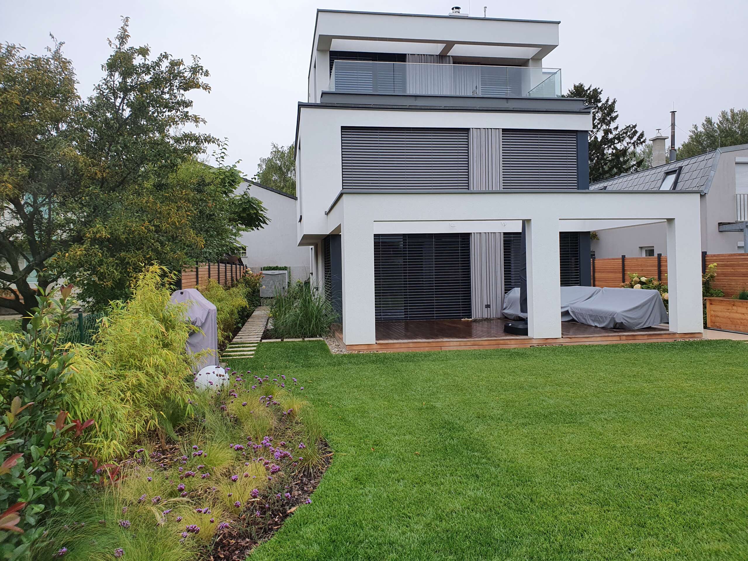 Moderner Privatgarten mit Rasenfläche, Holzdeck und moderner Bepflanzung – Gartengestaltung Wien