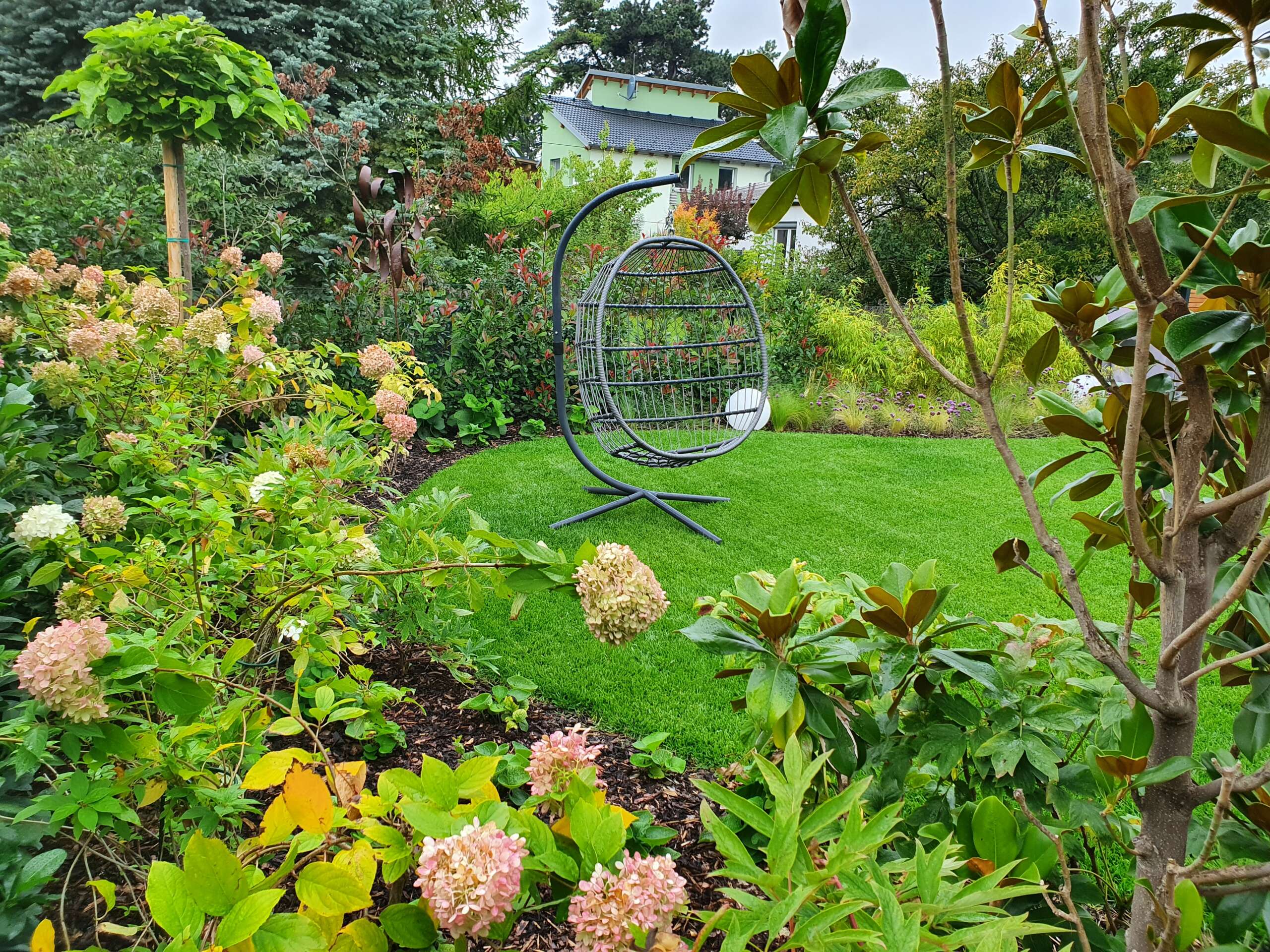 Blick durch die Bepflanzung auf einen modernen Familiengarten mit strukturreicher Pflanzung