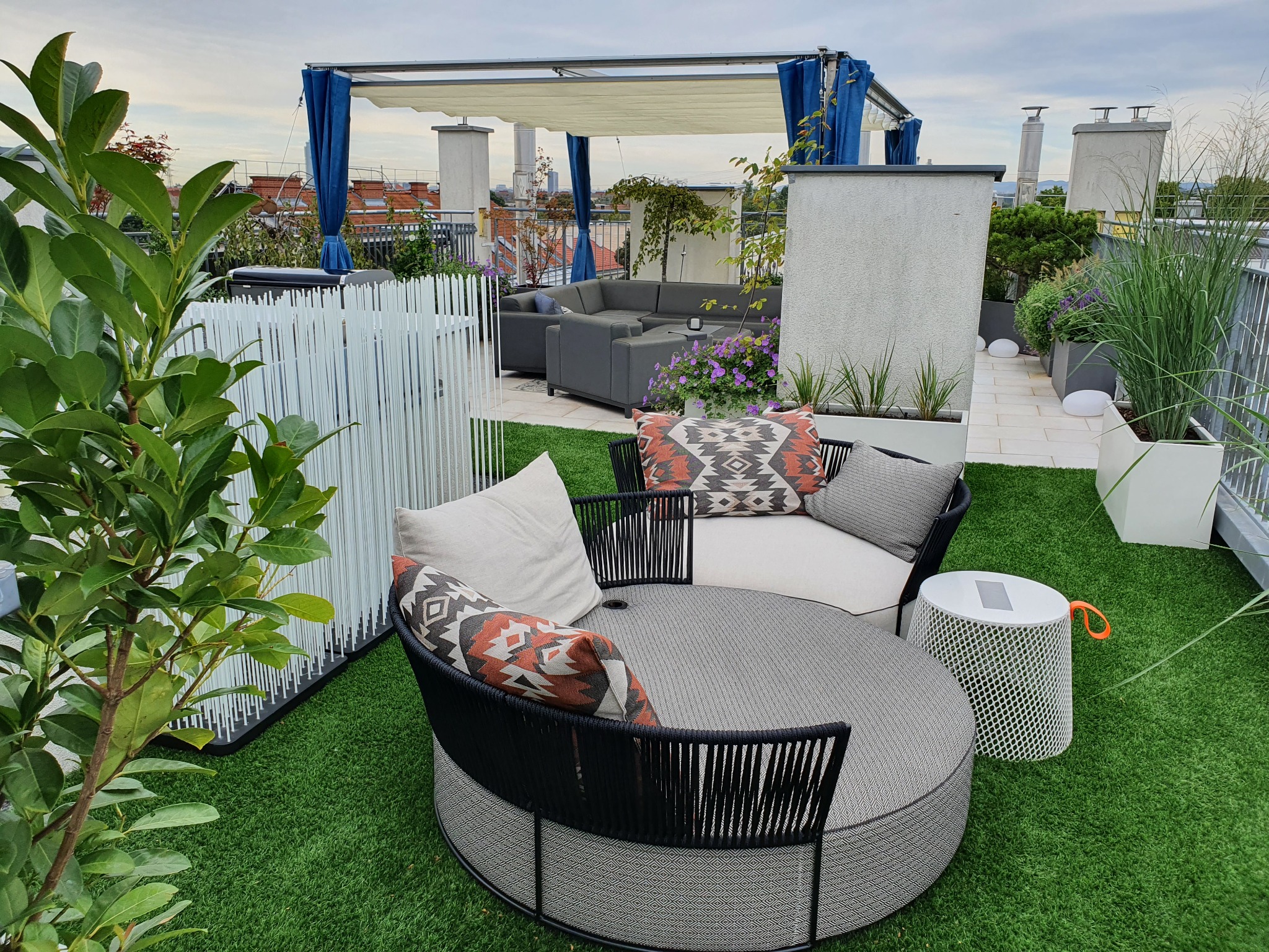 Modern gestaltete Dachterrasse mit runder Outdoor-Sitzgruppe, Kunstrasen und dekorativen Pflanztrögen