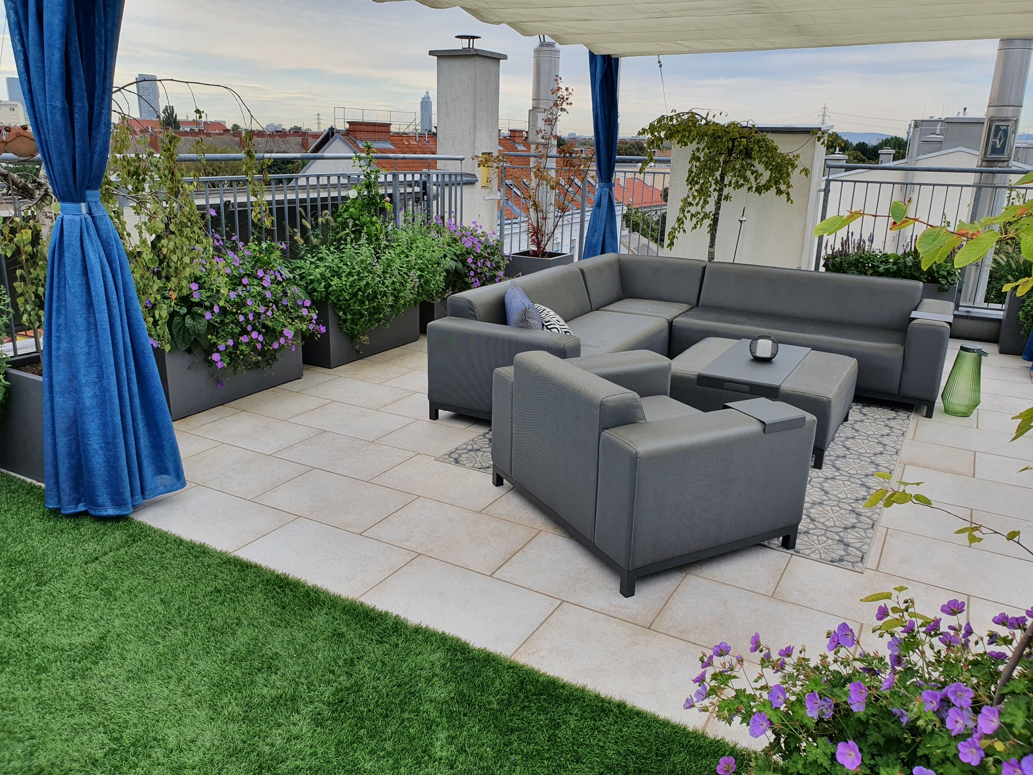 Dachterrassenbegrünung mit blühenden Stauden in anthrazitfarbenen Pflanztrögen und gemütlichen Loungemöbeln